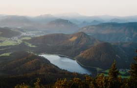 Blick vom Gipfel auf einen See mit Bergpanorama rundherum