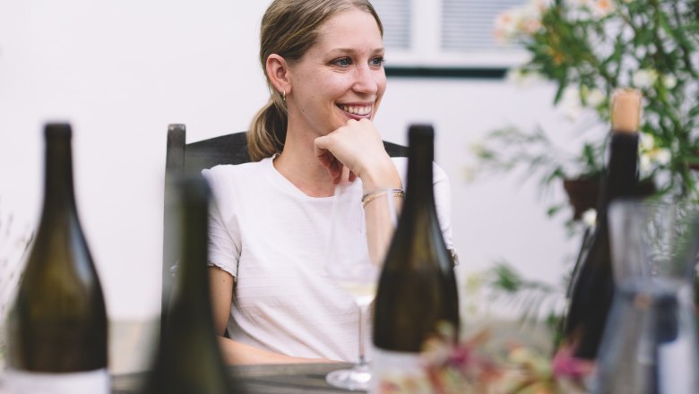 Winzerin Sophie Fidesser sitzt an einem mit Weinflaschen gefüllten Tisch 